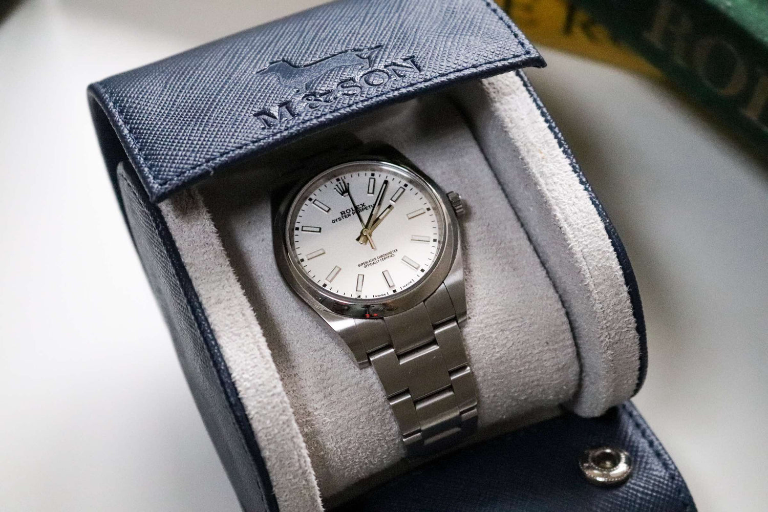 m and son royal blue saffiano watch roll with a rolex watch inside it - half open but still showing the m and son logo
