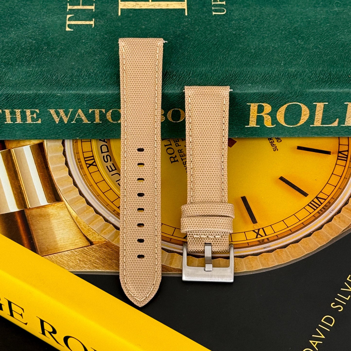 A sailcloth watch strap in desert tan color displayed on a watch with a green band and a yellow dial.