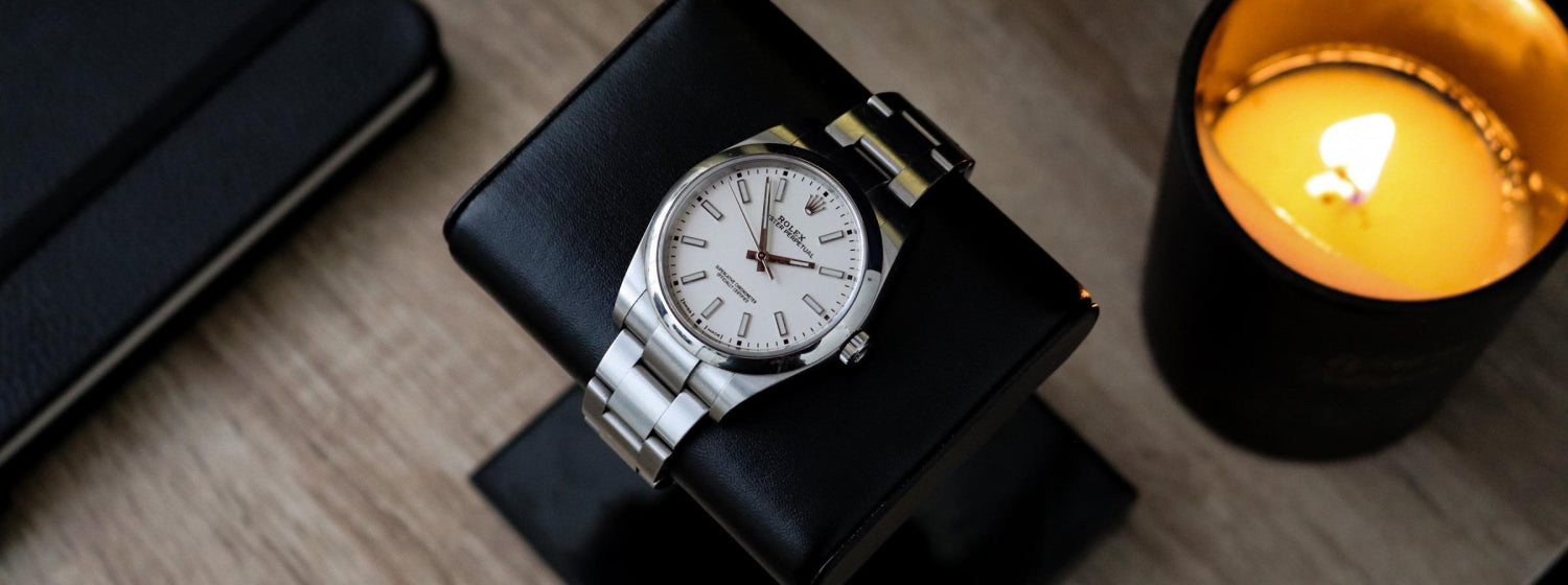 rolex watch on a black leather watch stand next to a lit candle