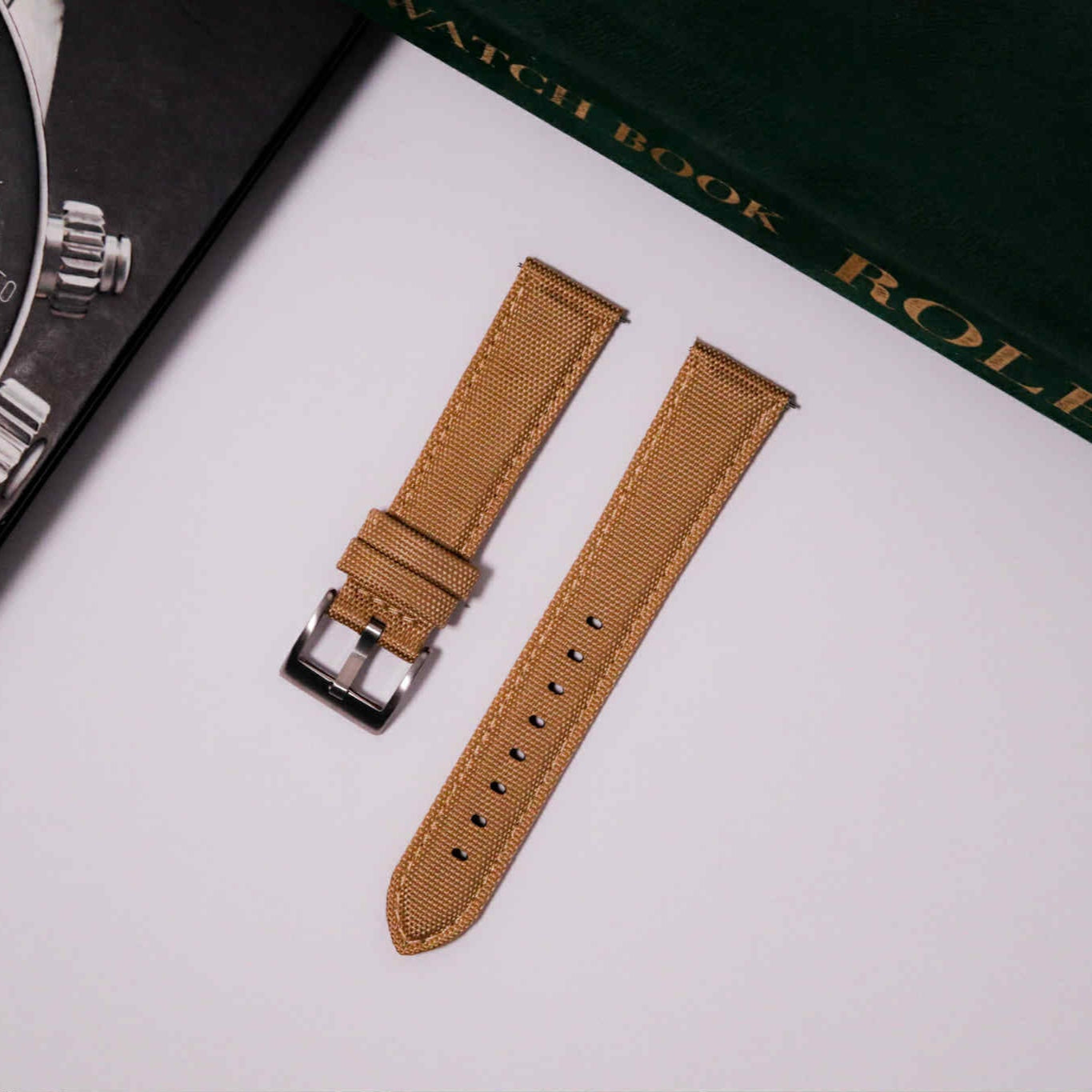 Brown watch strap on a white surface with a Rolex book in the background