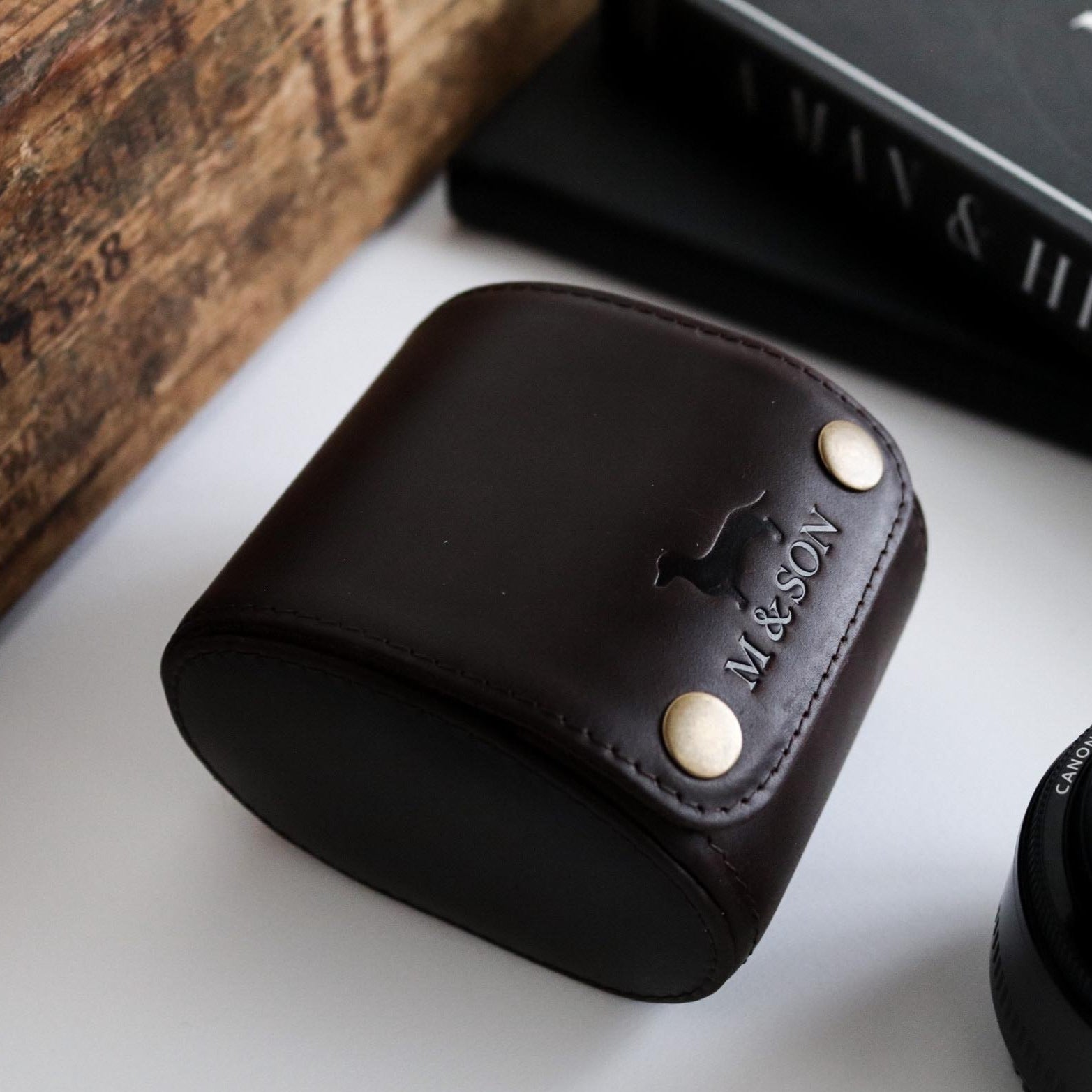 M and Son, leather watch roll with embossed logo on table, side view.