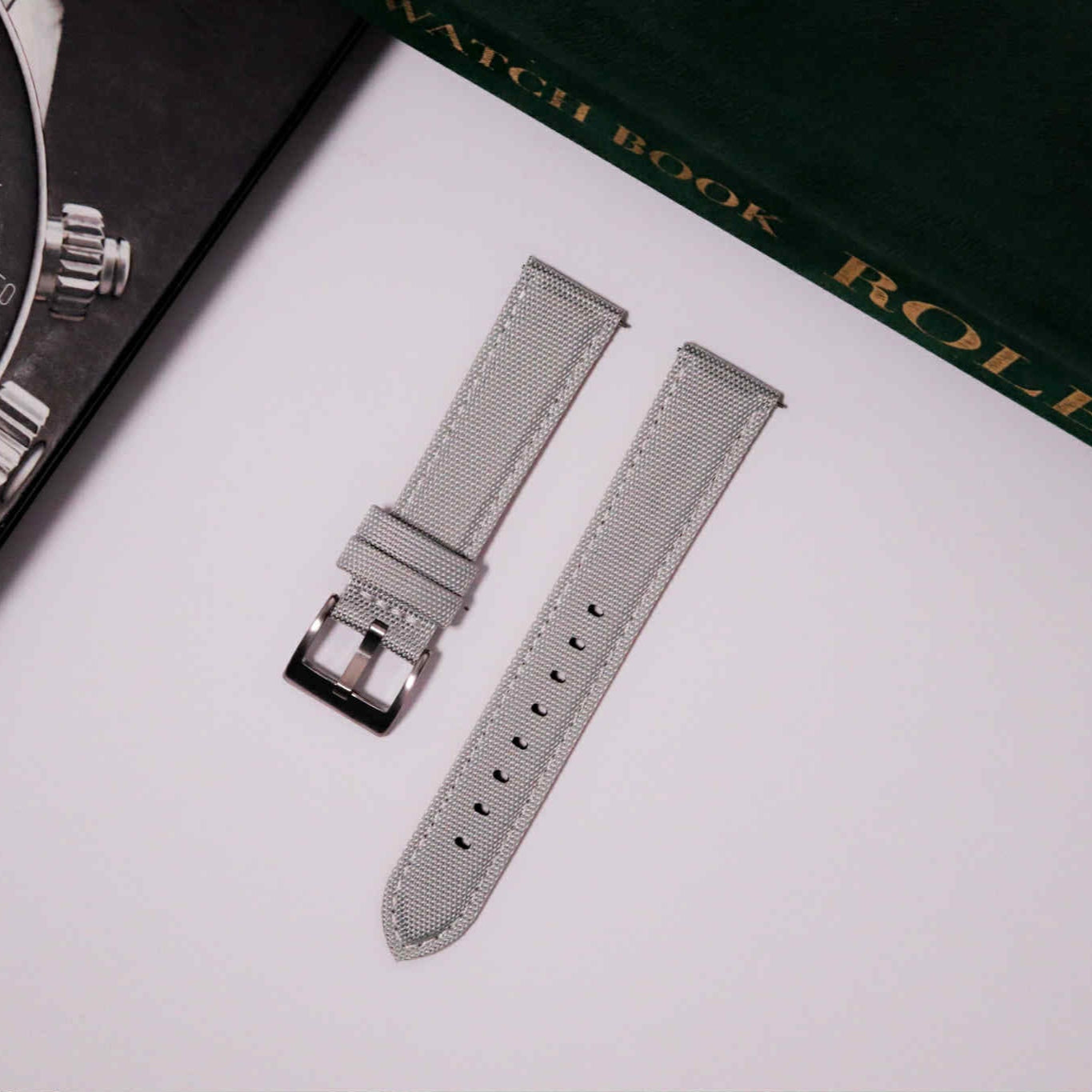 Silver watch strap on a white surface with a Rolex watch book in the background