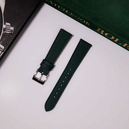 Green watch strap with silver buckle on a white surface with a Rolex box in the background.