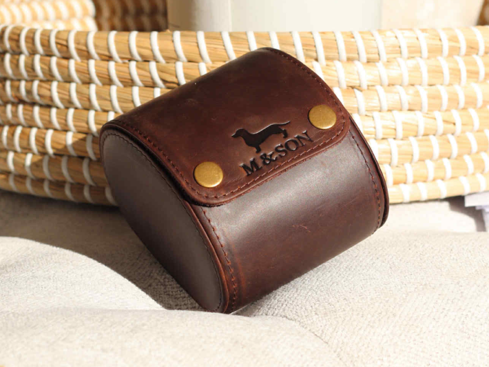 Brown leather watch case with 'M&Son' branding on a woven surface