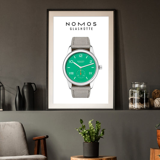 Framed poster of a Nomos Glashüte watch with green face and gray strap on a wall.