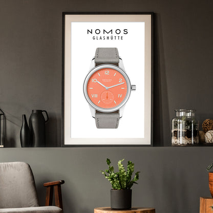 Framed poster of a Nomos Glashüte watch with a gray strap and coral face on a dark wall.