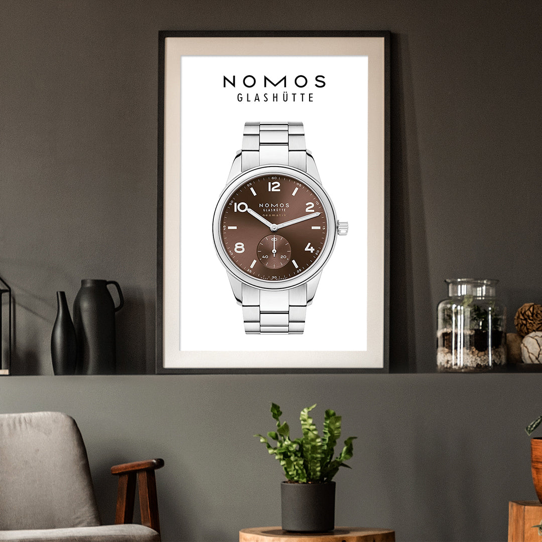 Framed poster of a Nomos Glashüte watch on a wall with decorative items.