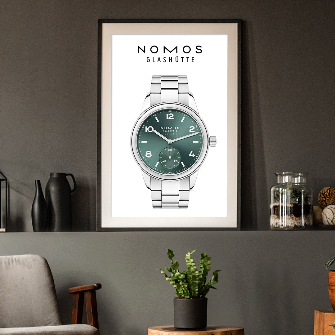 Framed poster of a Nomos Glashüte watch on a wall with decorative items.